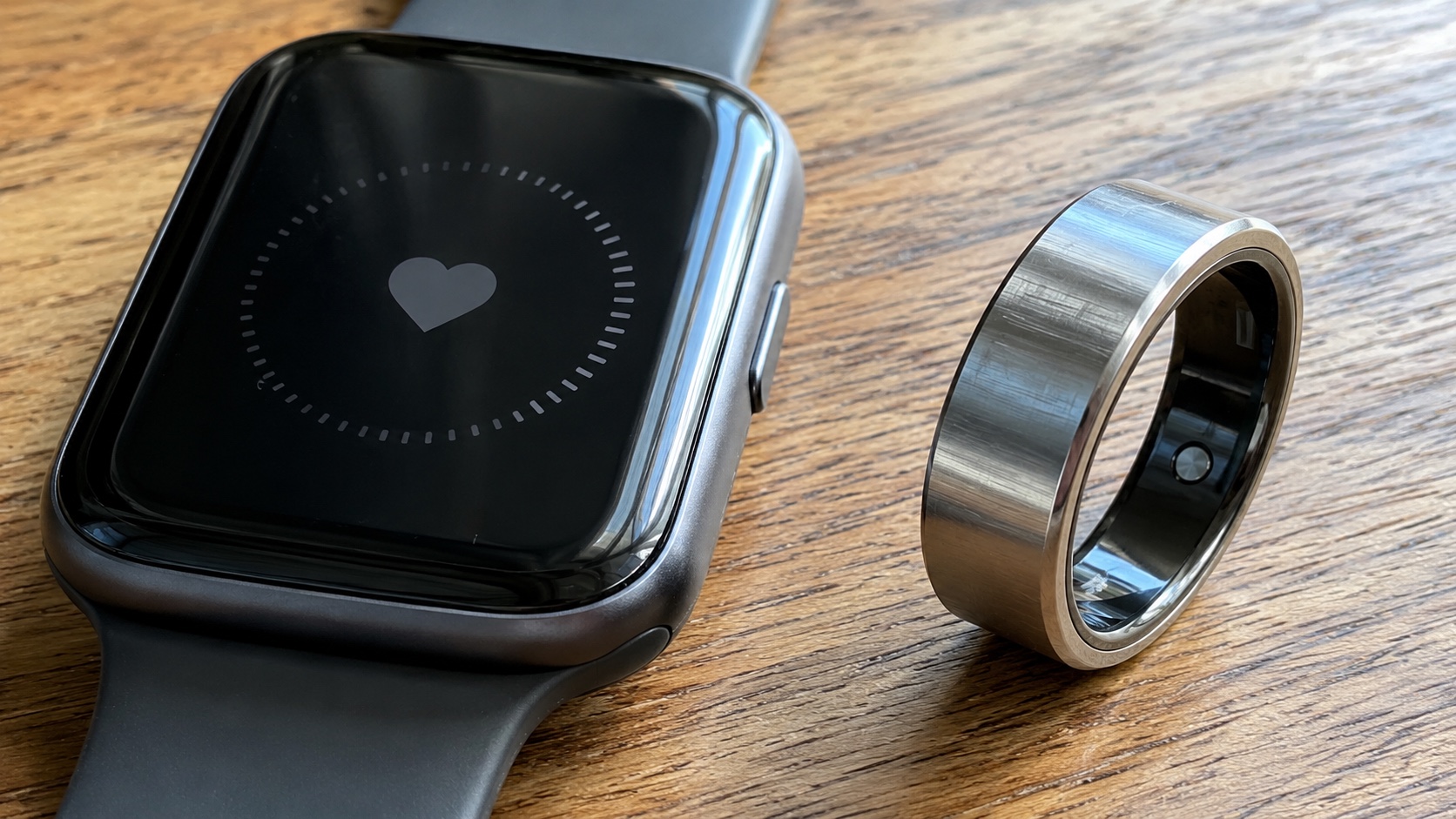 A smartwatch and smart ring side by side on a wooden table
